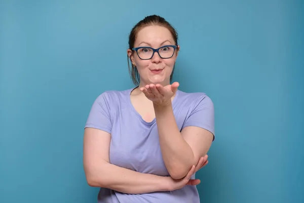 Зріла біла жінка в окулярах відправляє повітряний поцілунок на синьому фоні — стокове фото