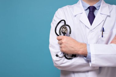 Mavi duvarda steteskoplu ve beyaz elbiseli bir doktor ya da stajyer.