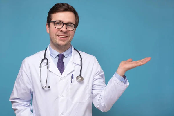 Young caucasian doctor with hand show on copyspace smiling and looking at camera — Stock Photo, Image