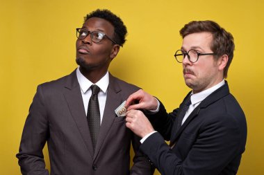 Takım elbiseli genç adam sarı arka planda iş ortağına rüşvet veriyor.