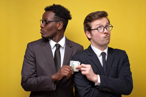 Young man in suit giving bribe to business partner on gyellow background. — Stock Photo, Image