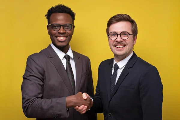 Два африканских и кавказских бизнесмена улыбаются и пожимают руки — стоковое фото