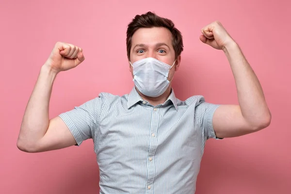 Caucásico joven sosteniendo puños hasta ser feliz con la recuperación usando máscara médica —  Fotos de Stock