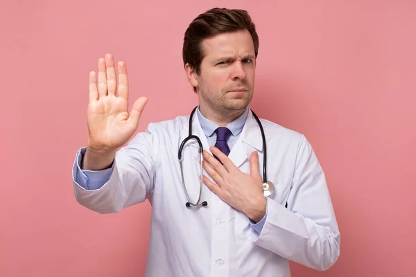 Ung stilig man i vit rock, praktikant eller läkare visar stopp med handen — Stockfoto