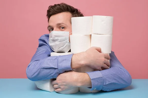 Excited caucasian man in medical mask is happy ge have a stock of toilet paper. Studio shot