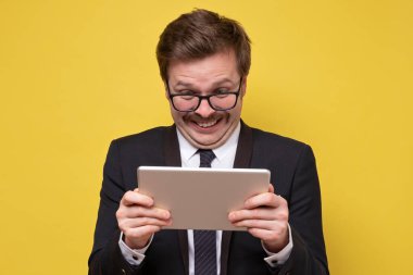 Gözlüklü, elinde dijital tablet kullanan, sosyal medya haberlerine şaşırmış, görüntülü sohbet yapan mutlu adam. Stüdyo çekimi