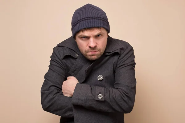 Junger kaukasischer Spekulant, Gangster oder Bandit, der wütend in die Kamera blickt und seinen Mantel schließt. Studioaufnahme — Stockbild Junger Kaukasischer Spekulant Gangster Oder Bandit Der Wütend Die Kamera — Stockfoto