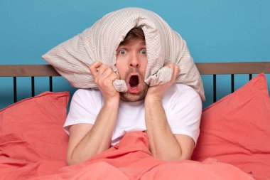 Cauacsian young man with pillow on head lying in bed and screaming being alone stressed because of quarantine clipart