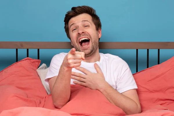 Сміючись Задоволений Чоловік Вказує Сидите Ліжку Ізольовані Синьому Фоні Спостерігаючи — стокове фото