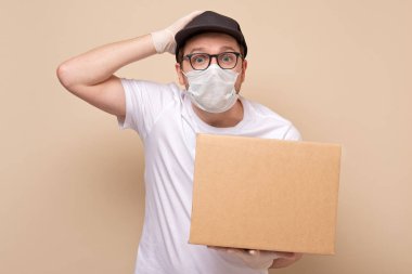 Panik halinde genç teslimatçı beyaz arka planda izole edilmiş bir kart kutusu tutuyor ve taşıyor.