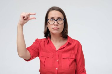 Bu çok küçük. Kırmızı gömlekli güzel olgun bir kadın parmaklarıyla küçük beden jest yapıyor. Küçük ödeme ya da maaş kavramı.