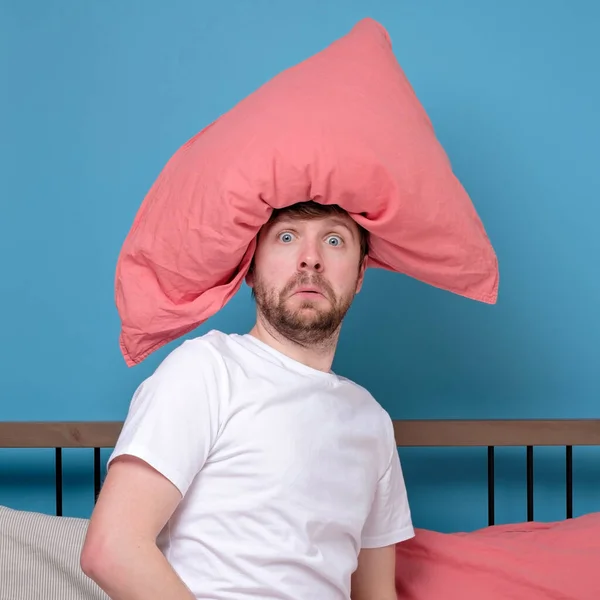 Cauacsian young man with pillow on head like hat having mental disorder being alone stressed because of quarantine