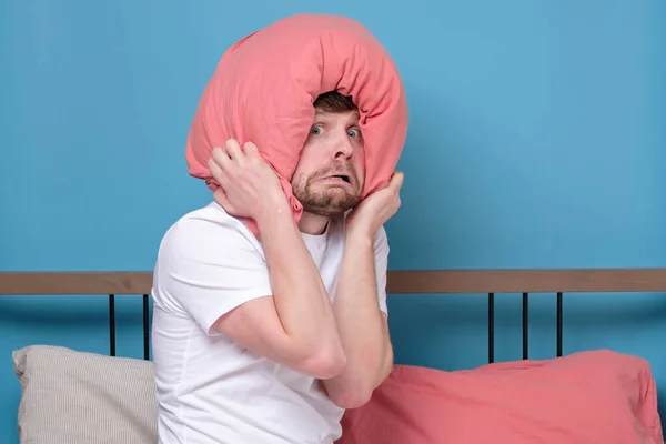 Cauacsian young man with pillow on head in bed being afraid being alone stressed because of quarantine
