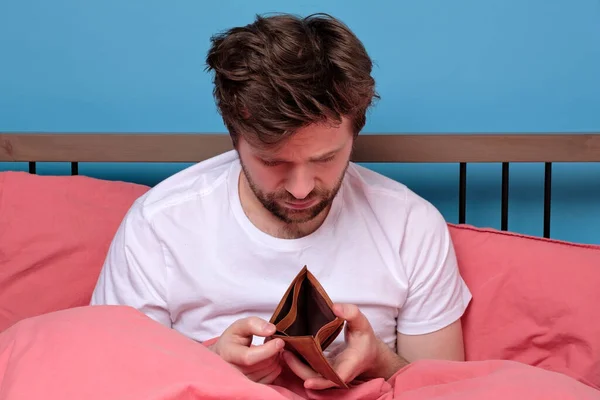 Poverty and absence of money. Unemployed sad caucasian man sitting at home showing empty wallet. He has no money for living.