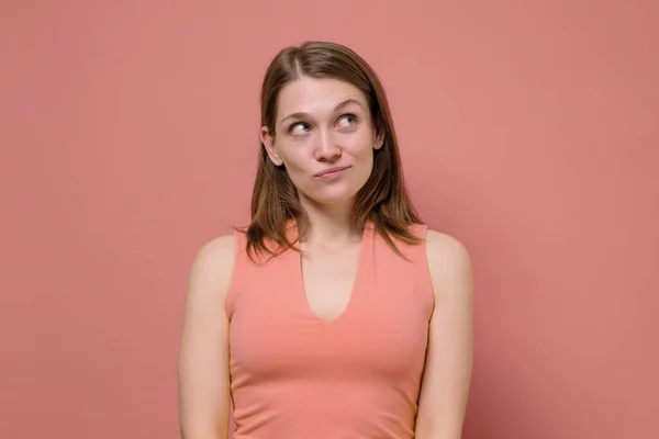 Young caucasian woman suspects something wrong being doubtful in friend telling whole truth, squinting suspicious at camera. Studio shot on colored wall. Studio shot