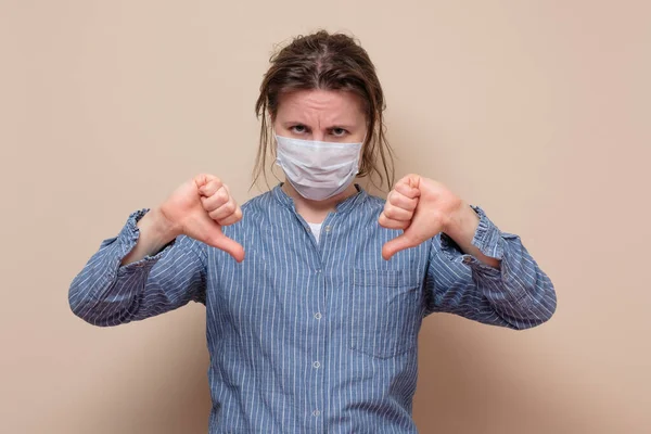 親指を示す医療用マスクの若い女性 スタジオで撃たれた 否定的な顔の人間の感情 — ストック写真