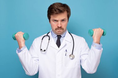 Beyaz önlüklü beyaz erkek doktor elinde dambıllar tutuyor. Spor ve diyet konsepti