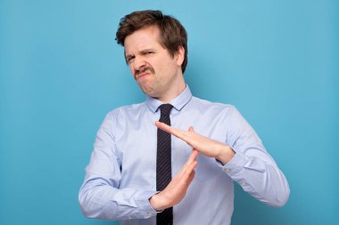 Genç ve yorgun bir adam mavi duvarda izole edilmiş el hareketi yapıyor. Yorgun adam ara vermek istedi..