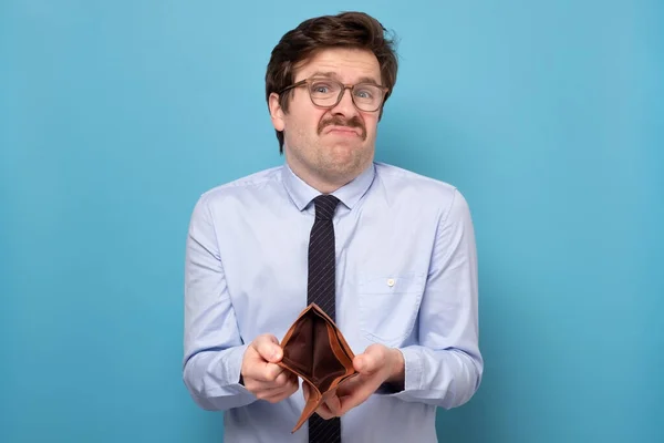 Sad businessman holding an empty wallet isolated on a blue background. — Stock Photo, Image