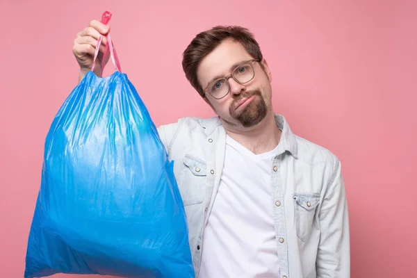 Hombre guapo sosteniendo bolsa de basura azul aislado sobre fondo rosa —  Fotos de Stock