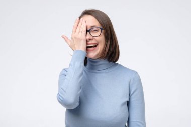 Gülen beyaz gözlüklü kadın yüzünü yarım eliyle beyaz duvara kapattı..