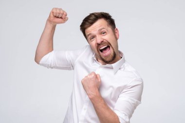 Beyaz arka plana karşı başarısını kutlamak için yumruklarını kaldıran heyecanlı beyaz adam. Stüdyo çekimi. Olumlu yüz insani duygu.