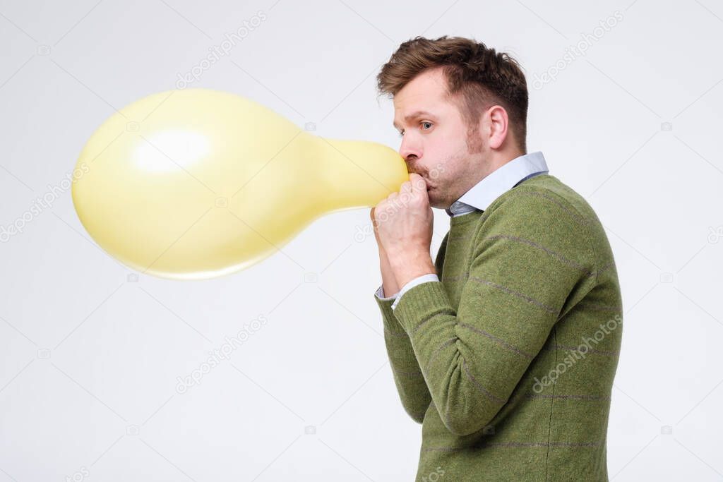 young man in green sweater inflating yellow balloon. Test on lungs strength.