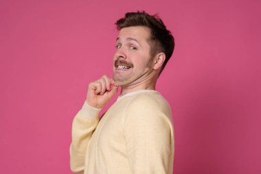 Çift çeneli, sarı tişörtlü genç adam. Uygunsuz diyetin sonucu olarak aşırı kilolu. Stüdyo resmi pembe duvarda..