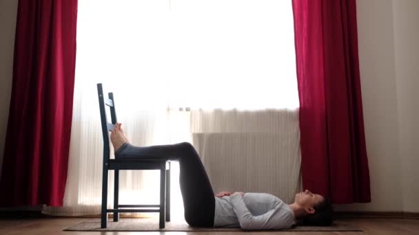 Jovem mulher caucasiana descansando segurando pernas na cadeira, relaxante asana respiração . — Vídeo de Stock