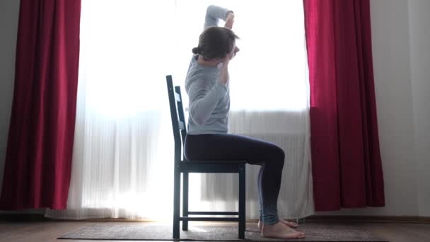 Mulher fazendo exercícios de aquecimento, flexão lateral com os braços levantados sentados na cadeira — Vídeo de Stock