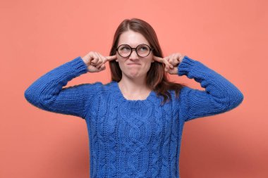 Gözlüklü genç bir kadın. Hoşnutsuz görünüyor. Kulaklarını tıkamış, gürültüden rahatsız oluyor.