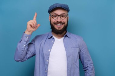 Yazlık mavi şapkalı sakallı adam bir şeyi işaret ediyor.