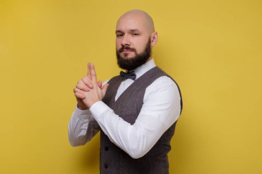 Sakallı bir adam ciddi ciddi kameraya bakıyor, silah taşıyormuş gibi yapıyor.