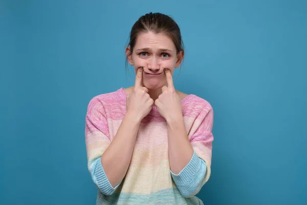 Jeune femme bouleversée faisant un faux sourire avec ses doigts étirant les coins de sa bouche — Photo