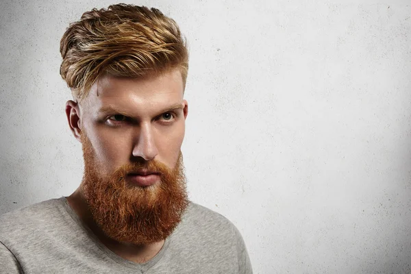 Portrait of young European hipster with fair skin and trendy ginger beard. Fashionable undercut hairstyle and handsome face features together with virile character make him look utterly attractive.