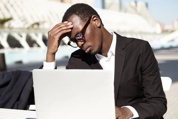 Tired black businessman working with laptop