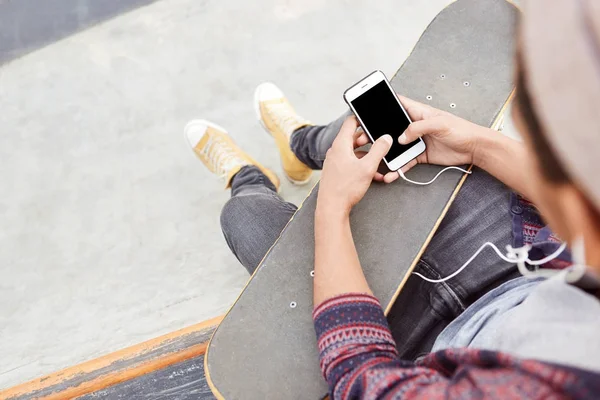 teenager holds skateboard, uses modern smartphone