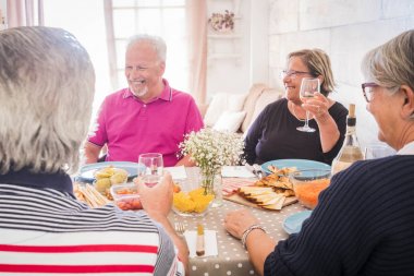 Yaşlı insanlar kıdemli grup birlikte gülen ve having fun peynir, havuç ve Meksika yemeği yemek mutfak kal. Parti ve güzel time.window arka ışık için şarap içmek