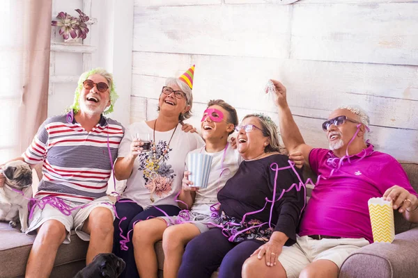 a group of elderly men with white hair, two men, two women, a boy and two little pugs spend time together. Play and laugh with disguises and colorful masks at home