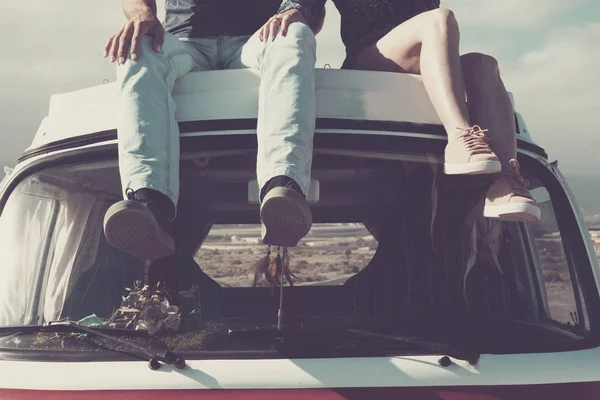 enjoy the vanlife. two pair of young legs sitting on the top of a vintage retro van enjoying the day. travel and discover new places like a desert in background. every morning new world wake up.