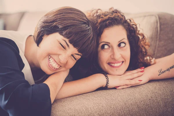 nice time and happiness with laugh and smiles for two caucasian friends lay down together on the sofa at home. friendship concept for indoor picture with window natural light