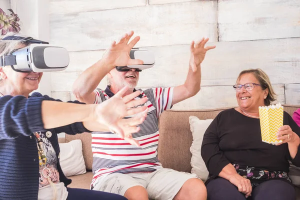 three senior try virtual reality technology at home. Sitting on the sofa smiling and laughing for the new experience when retired. Friendship concept