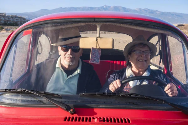 二人の先輩の男性と女性のための古い赤い車を運転 彼女の笑顔し 彼はあなたを見ています 帽子との両方 代替旅行の概念 — ストック写真