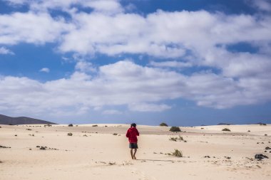kırmızı ceket fuerteventura Kanarya Adaları İspanya çölde niddle yürüme ile yalnız genç adam. çıplak ayak gibi Dağları ile ve hiçbir yerde çevresinde onu kaybettim. Mavi gökyüzü ve sarı kum.