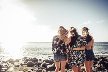 Üç genç güzel kız grup kucaklamak kendilerini tatil okyanus günbatımında bakarak. Takım an dolu duygular ve anılar. Mavi bir gökyüzü güneş ışığı.