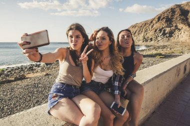 Üç kadın selfies alarak ve telefonunuzun ve plaja Tenerife yakın dostluk grubu. Günbatımı zamanı, gülümseme ve mutluluk içinde tatil çok. Güzel kızlar bağımsız hayattan zevk
