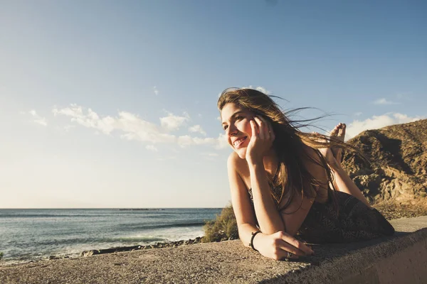 ビーチ近くの壁に長い髪スペイン若い女性リラックスが横たわった 彼女の美しさの顔に日光笑顔し 時間を楽しむ — ストック写真