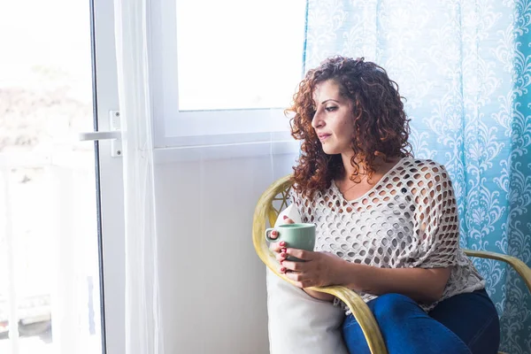one woman at home near the window with a cup of tea or coffee. bright light and thoughts for beautiful female in a clear house.