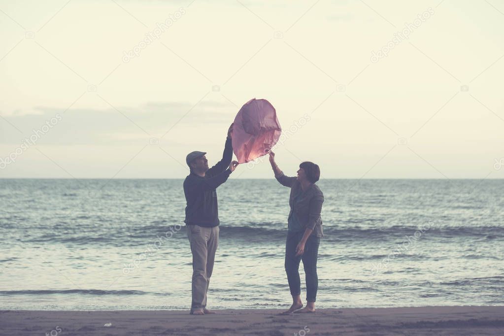 couple together forever dream and wish some desires, red Chinese lantern fly on the sky at the evening with ocean in the background. beach leisure activity in vacation, love concept