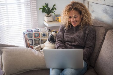 Kanepede kişisel bilgisayarını kullanan komik köpekli yetişkin bir kadın. 
